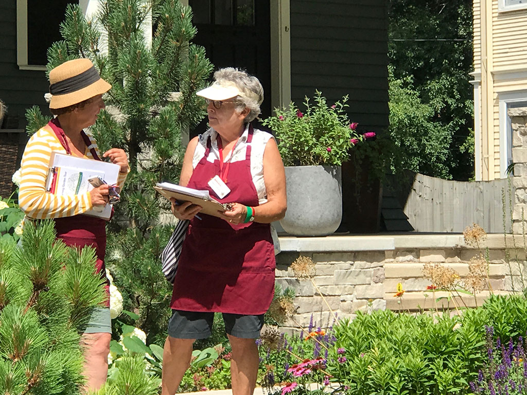 Two women wearing sun hats, standing in a garden and talking.